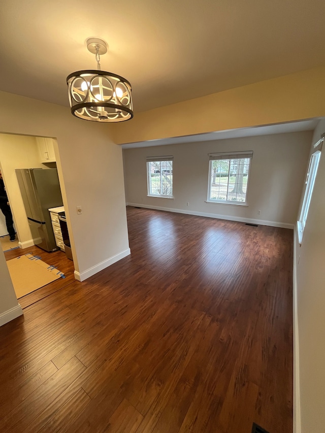 unfurnished room with a chandelier, dark wood-type flooring, and baseboards