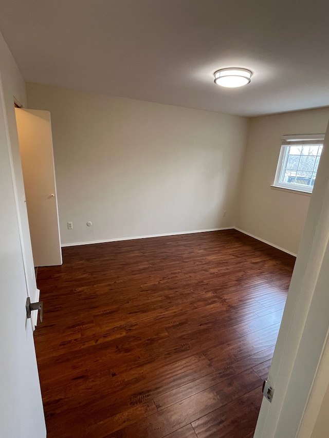 spare room featuring baseboards and dark wood-style flooring