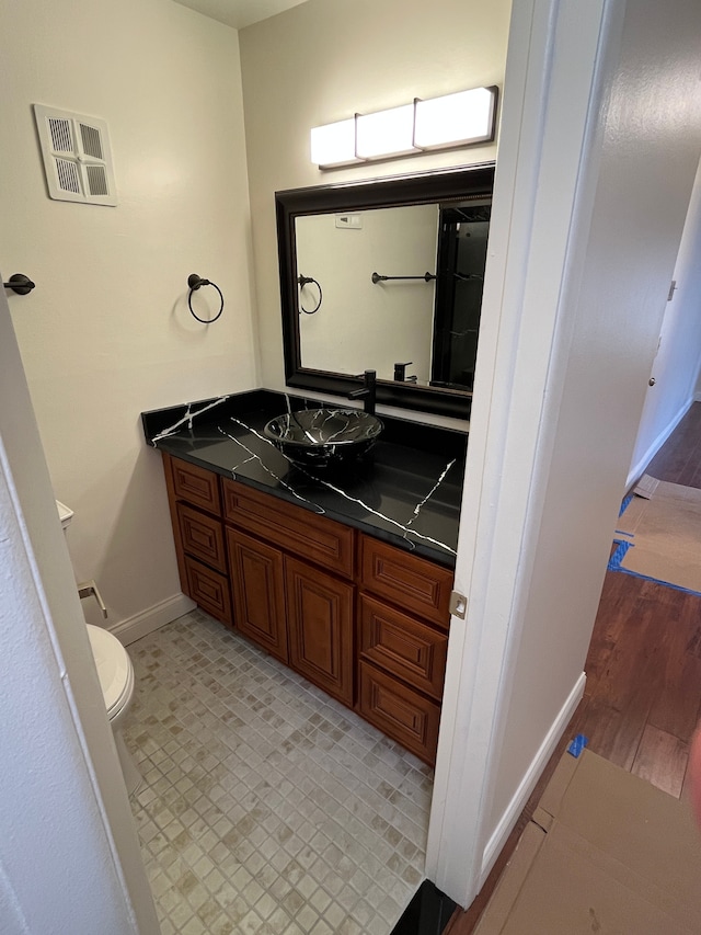 half bathroom with baseboards, visible vents, vanity, and toilet