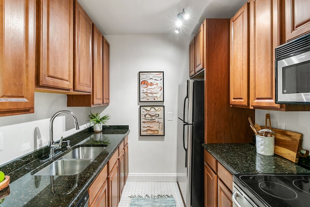 kitchen with stainless steel appliances, brown cabinetry, a sink, dark stone counters, and baseboards