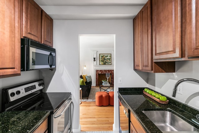 kitchen featuring a fireplace, stainless steel appliances, a sink, dark stone countertops, and wood finished floors