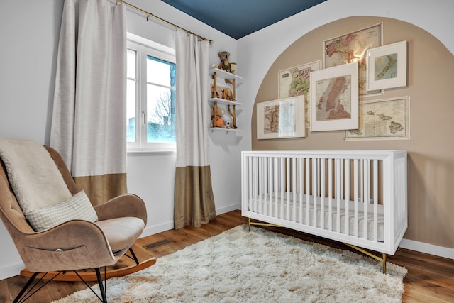 bedroom featuring visible vents, a crib, baseboards, and wood finished floors