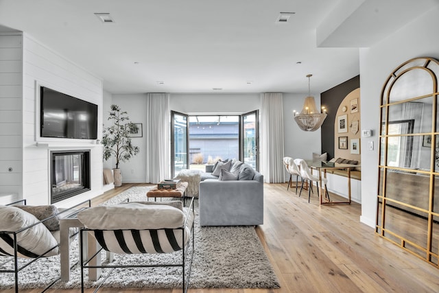 living room with baseboards, visible vents, a glass covered fireplace, hardwood / wood-style floors, and an inviting chandelier