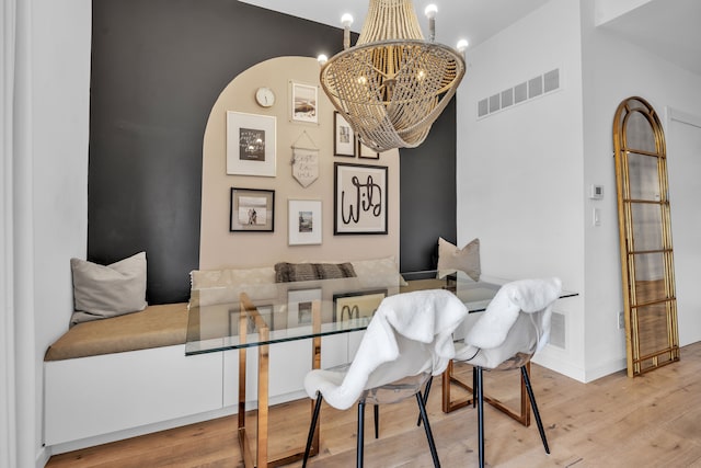 dining space with a chandelier, arched walkways, wood finished floors, visible vents, and baseboards