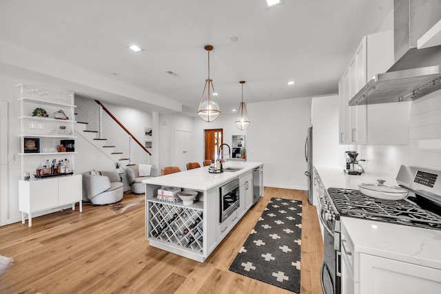 kitchen with white cabinets, wall chimney exhaust hood, appliances with stainless steel finishes, open shelves, and a sink