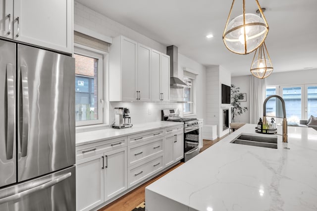 kitchen featuring tasteful backsplash, appliances with stainless steel finishes, wall chimney range hood, white cabinetry, and a sink