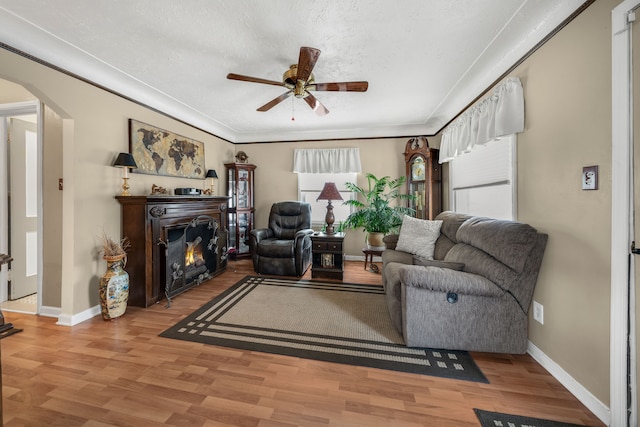 living room with light wood finished floors, a lit fireplace, arched walkways, and baseboards