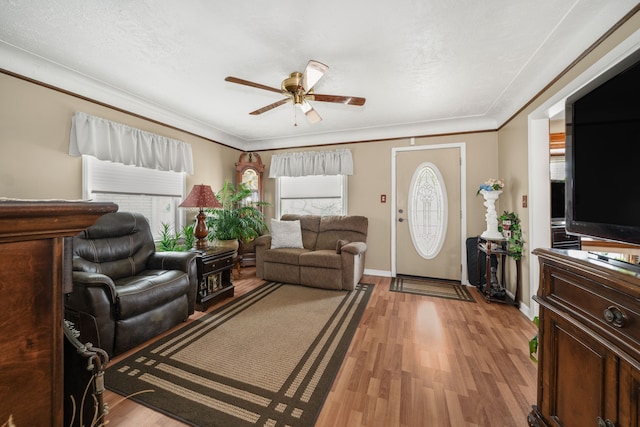 living area with light wood-type flooring, baseboards, ornamental molding, and a ceiling fan