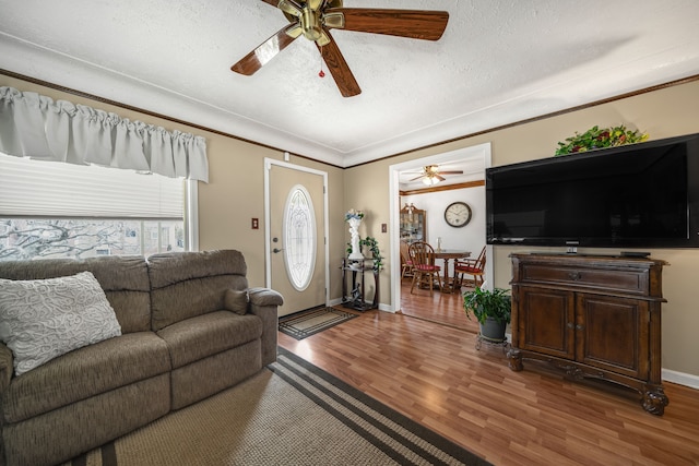 living room with crown molding, a ceiling fan, a textured ceiling, wood finished floors, and baseboards