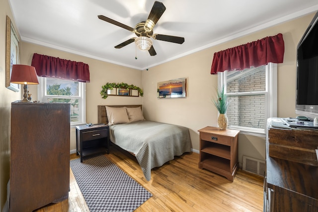 bedroom with ceiling fan, light wood-style flooring, visible vents, baseboards, and ornamental molding