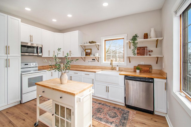 kitchen featuring butcher block counters, a sink, appliances with stainless steel finishes, open shelves, and light wood finished floors