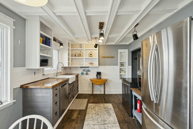 kitchen featuring appliances with stainless steel finishes, dark wood-style flooring, beamed ceiling, open shelves, and a sink