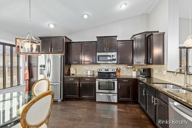 kitchen featuring stainless steel appliances, dark brown cabinetry, vaulted ceiling, a sink, and dark stone counters