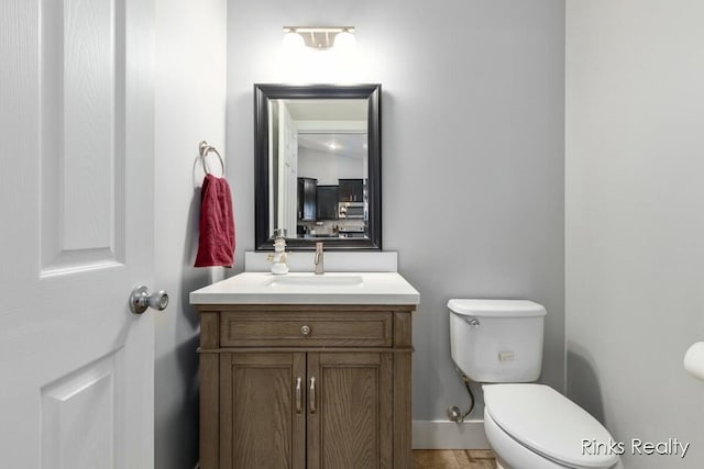 half bath featuring toilet, baseboards, and vanity