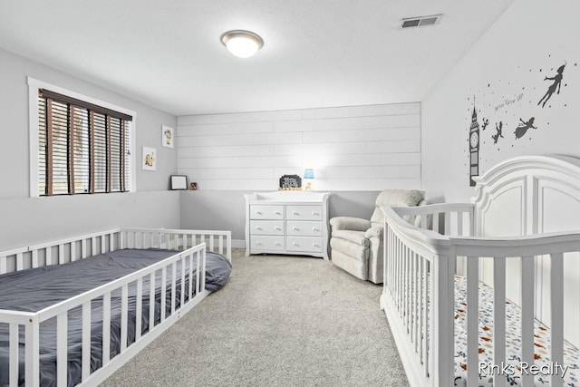 carpeted bedroom with a crib, wooden walls, and visible vents