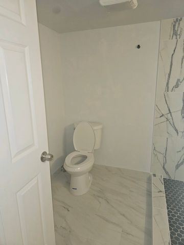 full bath with marble finish floor, walk in shower, and toilet