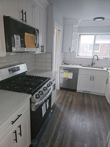 kitchen featuring white cabinets, ornamental molding, appliances with stainless steel finishes, decorative backsplash, and dark wood finished floors