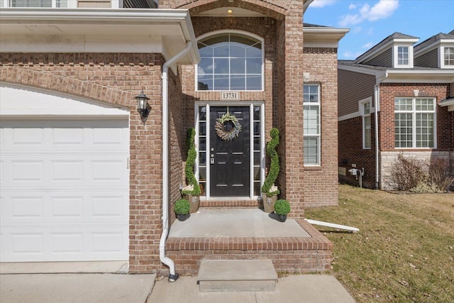 doorway to property featuring brick siding, an attached garage, and a yard