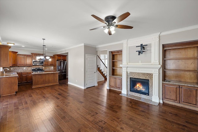 unfurnished living room with baseboards, dark wood-style flooring, a high end fireplace, a sink, and ceiling fan with notable chandelier