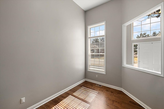 empty room with dark wood-style floors, visible vents, and baseboards