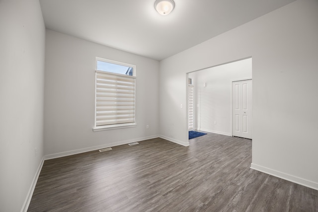 empty room featuring visible vents, dark wood finished floors, and baseboards