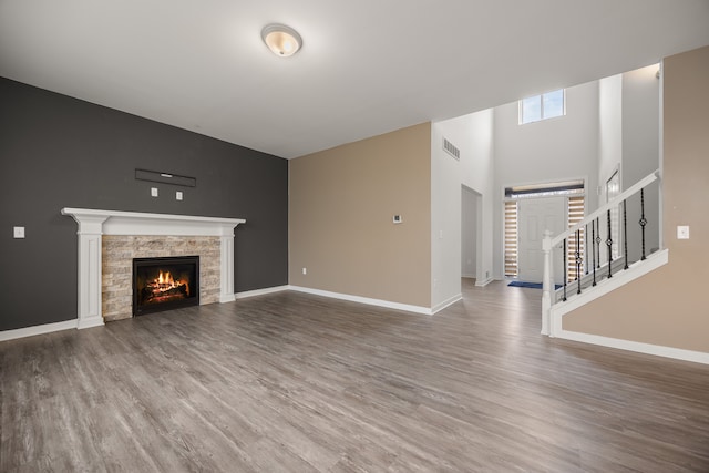 unfurnished living room featuring a warm lit fireplace, wood finished floors, stairs, and visible vents