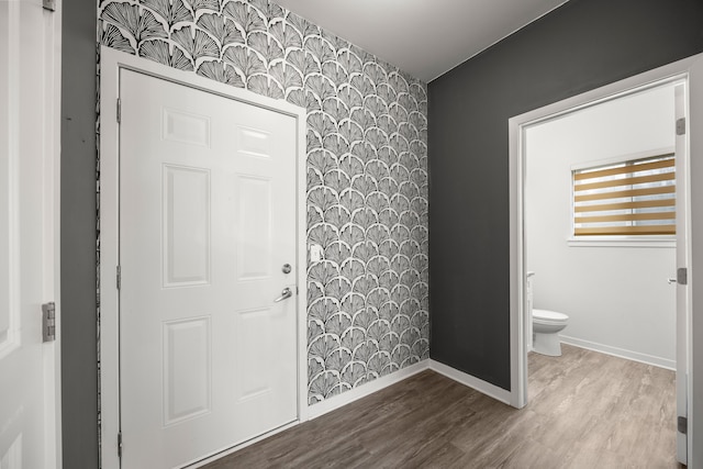 entryway with baseboards, an accent wall, wood finished floors, and wallpapered walls