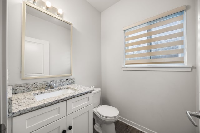 half bath featuring a wealth of natural light, vanity, toilet, and wood finished floors