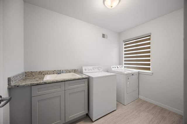 clothes washing area with light wood finished floors, baseboards, visible vents, washing machine and clothes dryer, and a sink