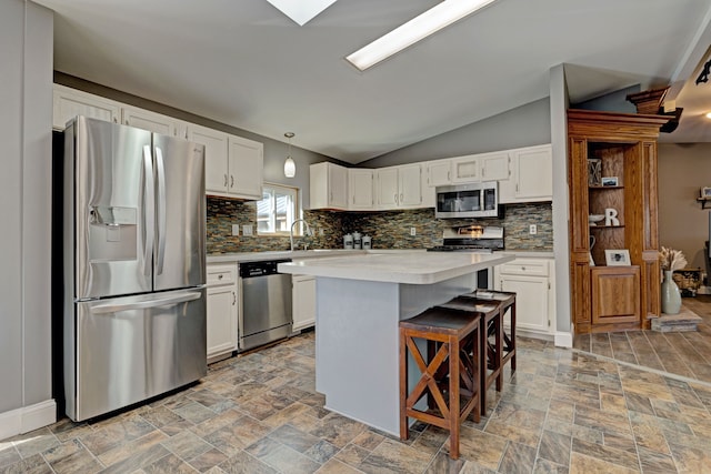 kitchen with appliances with stainless steel finishes, stone finish floor, white cabinets, and a kitchen island