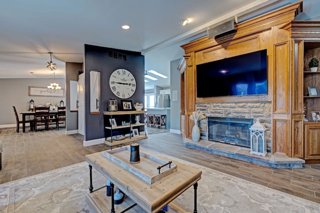 living room with wood tiled floor, a fireplace, baseboards, and an inviting chandelier