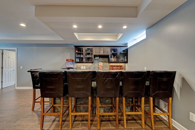 bar with backsplash, bar, a raised ceiling, and baseboards