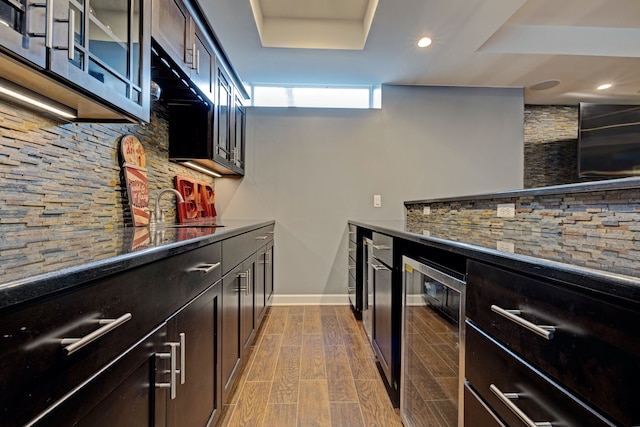 kitchen with wine cooler, wood finish floors, tasteful backsplash, glass insert cabinets, and a sink