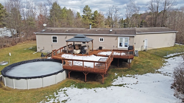 snow covered back of property featuring french doors, a covered pool, a gazebo, a deck, and a yard