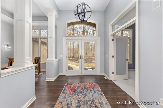 foyer entrance with a chandelier, dark wood-style flooring, french doors, and ornate columns