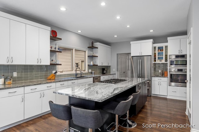 kitchen featuring a center island, open shelves, appliances with stainless steel finishes, a sink, and a kitchen bar