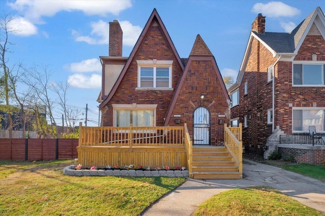 english style home featuring a chimney, fence, a front lawn, and brick siding