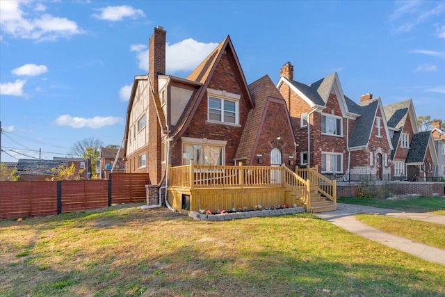 tudor house featuring a deck, a front lawn, fence, and brick siding