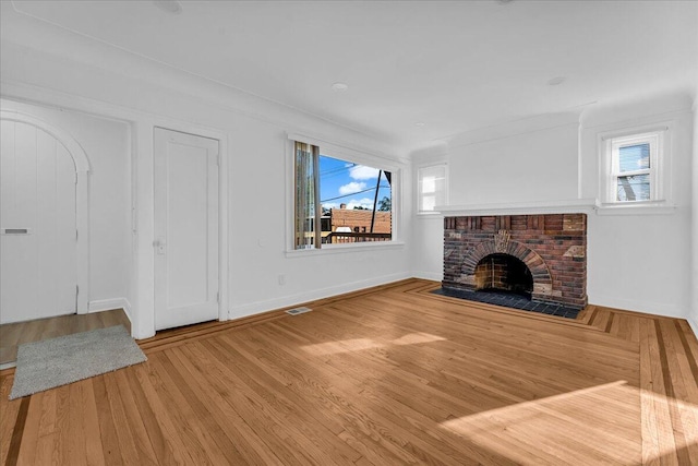 unfurnished living room featuring a brick fireplace, baseboards, visible vents, and wood finished floors