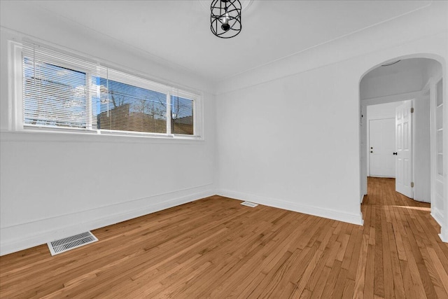 empty room with light wood-style flooring, visible vents, arched walkways, and baseboards