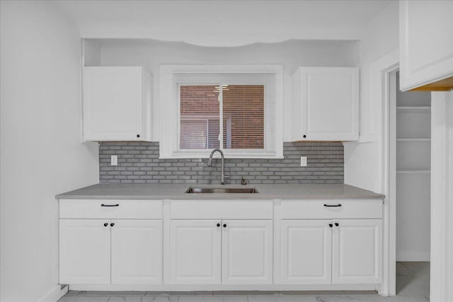 kitchen featuring white cabinets, decorative backsplash, light countertops, and a sink