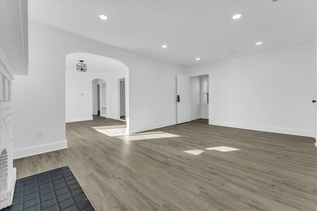 interior space featuring baseboards, arched walkways, wood finished floors, and recessed lighting