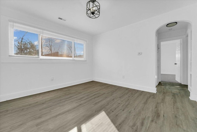 spare room featuring arched walkways, plenty of natural light, baseboards, and wood finished floors