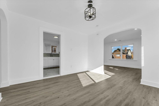 interior space with arched walkways, a sink, baseboards, and wood finished floors