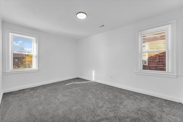 empty room with visible vents, dark carpet, and baseboards