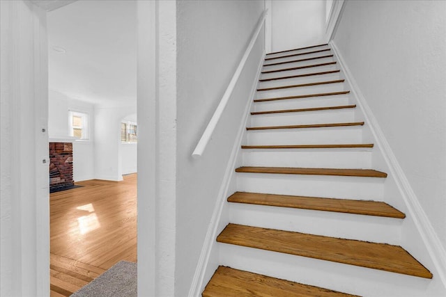 staircase featuring arched walkways, a brick fireplace, and wood finished floors