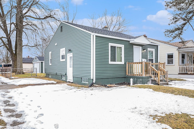 bungalow-style home featuring a garage, a shingled roof, a chimney, an outbuilding, and fence