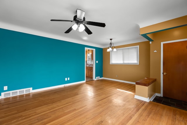 empty room with ceiling fan with notable chandelier, light wood-type flooring, visible vents, and baseboards