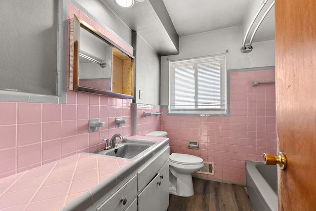 full bath with tile walls, visible vents, toilet, vanity, and wood finished floors