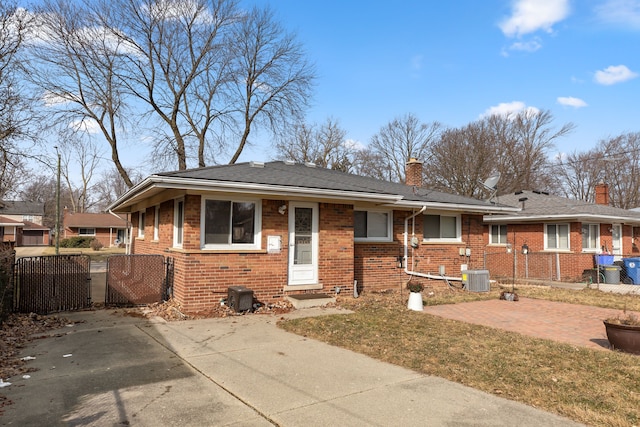 view of front of house featuring a chimney, a gate, fence, central AC, and brick siding